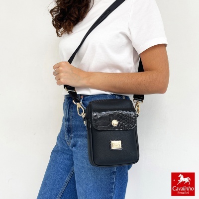 Mala pequena preta com detalhe em pele imitação cobra usada por mulher com t-shirt branca e jeans