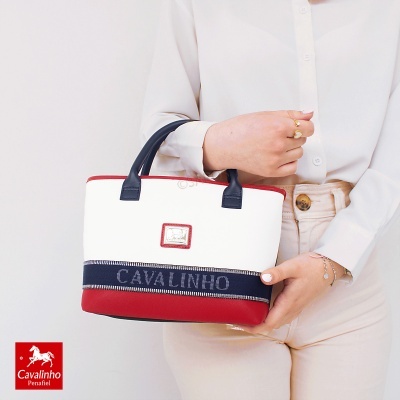 Mala de mão branca, vermelha e azul escuro com texto CAVALINHO, segurada por pessoa em roupa clara