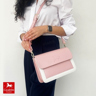 Mala rosa claro e branca de senhora com padrão em relevo de cavalo, alça ajustável, usada num contexto branco por pessoa vestindo camisa branca e calças escuras
