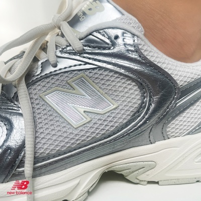 Ténis New Balance branco e prateado com sola branca em fundo branco