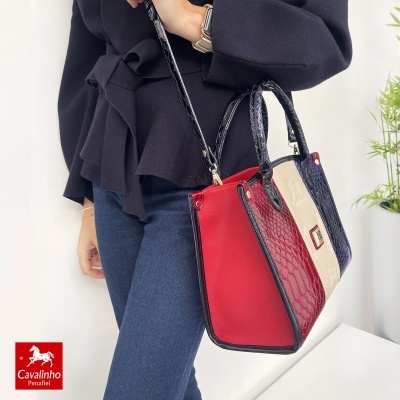 Mala Cavalinho Penafiel vermelha, branca e azul escuro com textura de pele de crocodilo, em ambiente interior.