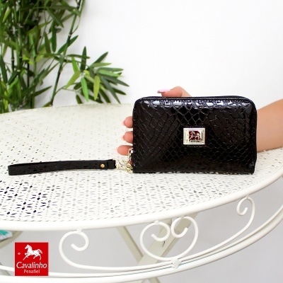 Carteira preta com padrão reptiliano e placa Cavalinho Penafiel sobre mesa branca