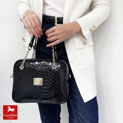 Mala preta textura pele crocodilo com alças de corrente dourada e logótipo Cavalinho, em modelo com blazer branco e calças azuis