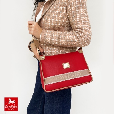 Mala bandoleira vermelha com detalhes bege e logo Cavalinho, vista lateral num fundo branco