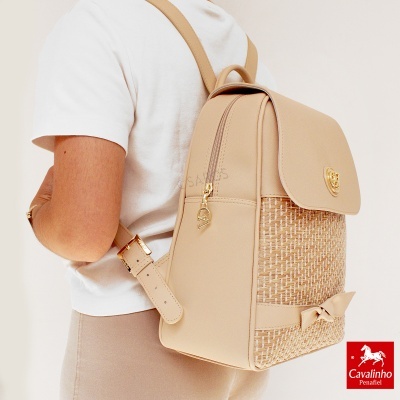 Mochila bege com padrão trançado e laço, detalhes dourados, usada por pessoa com camiseta branca.