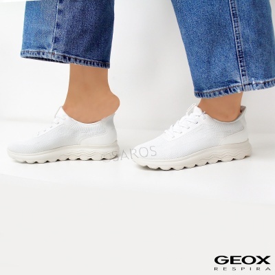 Ténis brancos de malha com sola ondulada e calças de ganga azul