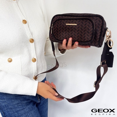 Bolsa marrom com padrão geométrico e detalhes dourados com alça larga, segurada por pessoa com casaco branco e jeans
