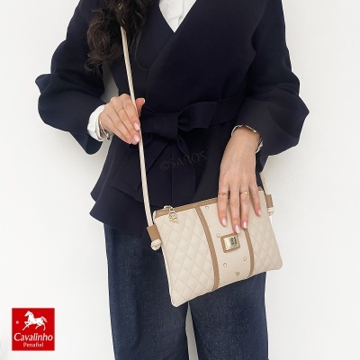 Mala bege claro matelassé com detalhes castanhos e fivela dourada da Cavalinho, usada por mulher com casaco preto e calças escuras
