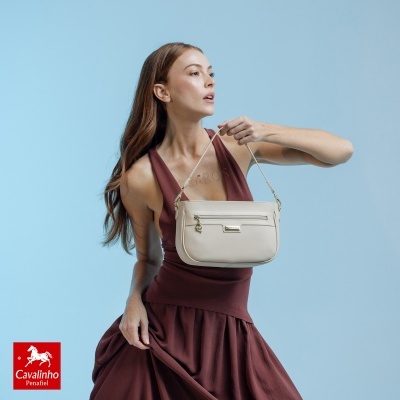 Mulher com vestido castanho segurando mala bege Cavalinho com fundo azul