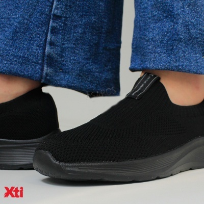 Ténis desportivos negros em tecido malha com sola preta e calças de ganga azuis