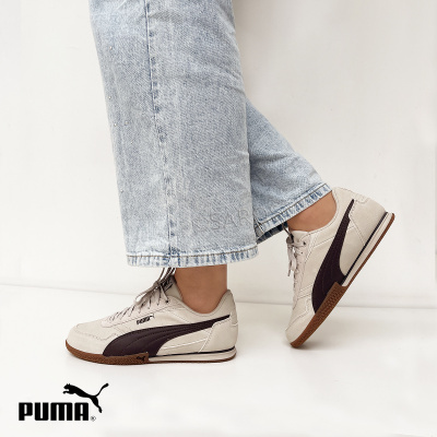 Tênis Puma bege com detalhes castanhos e calças de ganga claras.