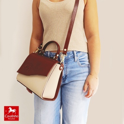 Mala de senhora castanha e bege com alças, usada por pessoa com camisola bege e jeans.