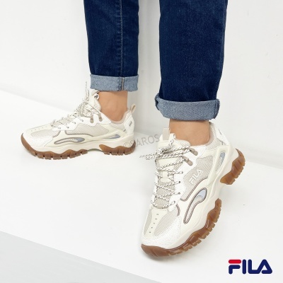 Ténis brancos com sola grossa castanha e marca FILA em ambiente neutro