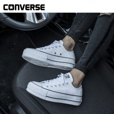 Sapatilhas Converse brancas de lona com sola plataforma, usadas dentro de um carro
