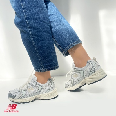 Ténis New Balance 530 brancos com detalhes cinza e sola creme usados com calças de ganga azul