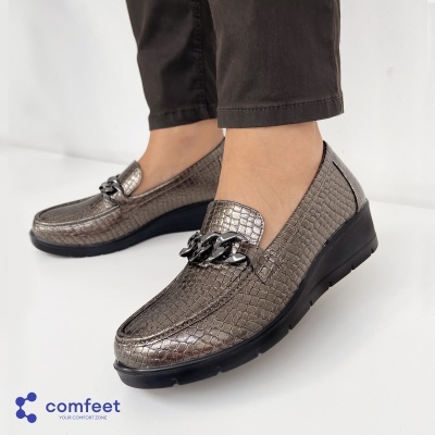 Mocassins metálicos cinza com padrão texturizado e corrente preta, solado preto, usados com calças castanhas.