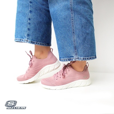 Ténis rosas Skechers com sola branca usados com jeans azuis.