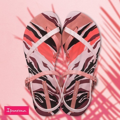 Sandálias Ipanema com padrão animal print e tiras cor de rosa claro numa superfície rosa com sombra de palmeira