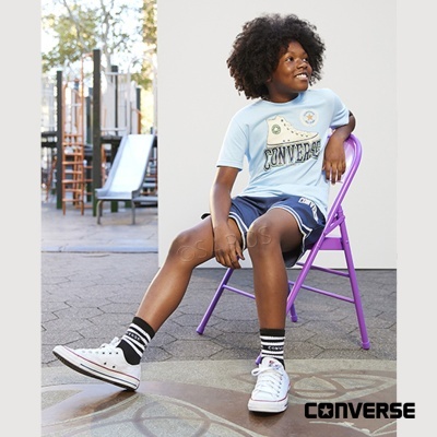 Criança sentada numa cadeira roxa ao ar livre com roupa Converse