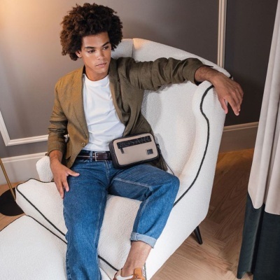 Homem com bolsa sentado numa poltrona branca com linhas pretas