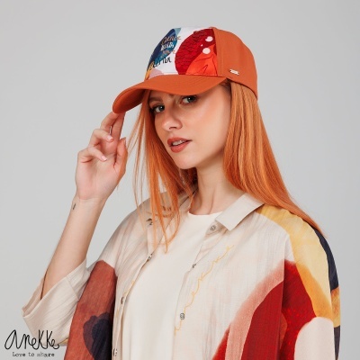 Mulher ruiva a usar boné tricolor com padrão gráfico e camisa estampada colorida em fundo cinza claro