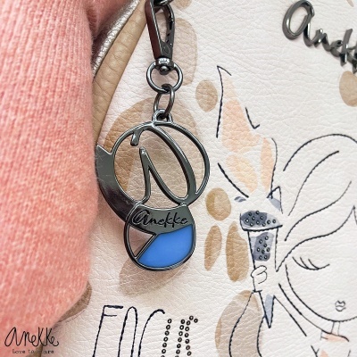 Chaveiro preto e azul pendurado em bolsa bege com padrão de bolinhas castanhas e ilustração feminina