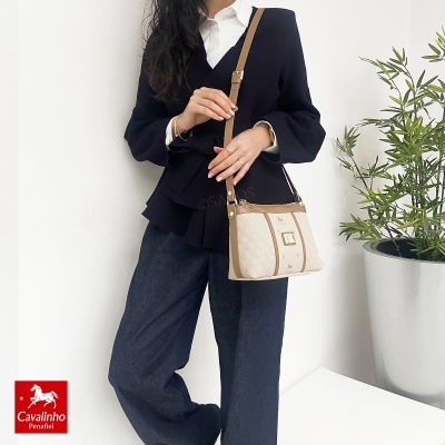 Mulher com mala bege e blazer preto junto a planta num vaso prateado