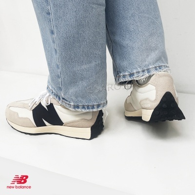 Sapatilhas New Balance bege, branco e preto com sola preta usadas com calças de ganga azul claro em fundo branco