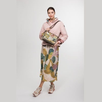 Mulher com casaco rosa, saia e malha coloridos, sapatos multicoloridos, segurando mala bege com padrão