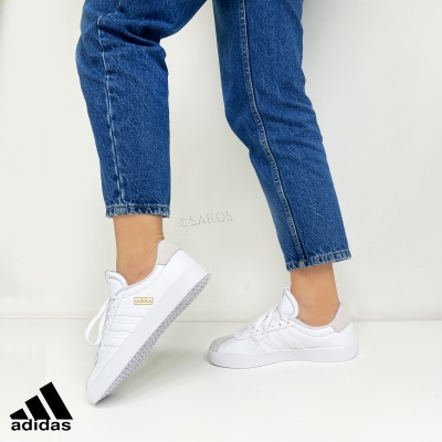 Ténis brancos Adidas com riscas usados com jeans azuis