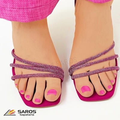 Sandálias rosa choque com tiras finas brilhantes e unhas pintadas rosa, fundo branco