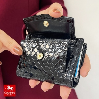 Carteira preta lacada com padrão tipo escamas e fecho dourado segurada por uma mão