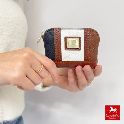 Carteira pequena de três cores com fecho e placa dourada, segurada por mão com anéis