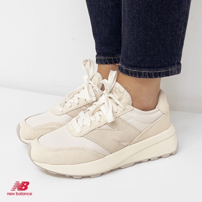 Ténis New Balance creme com atacadores brancos e sola branca vistos de lado com fundo branco
