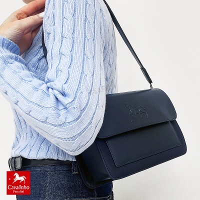 Mala de ombro azul escura em pele com relevo de cavalo e pessoa vestindo camisola azul clara de malha