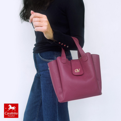 Mala vinho de pele Cavalinho com logótipo C&V dourado numa mulher com camisola preta e jeans.
