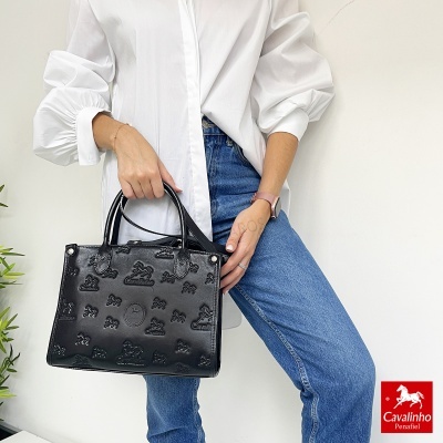 Bolsa preta de mão com padrão em relevo, exibida por pessoa com roupa branca e jeans azuis