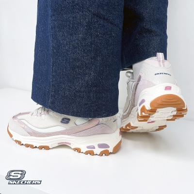 Ténis Skechers em branco, bege e rosa claro com sola antiderrapante, usados com calças de ganga azuis.