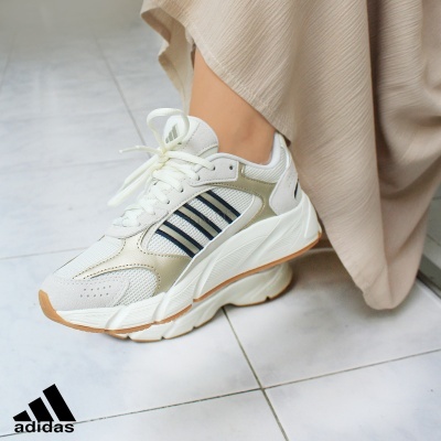 Ténis Adidas brancos e bege com riscas pretas, sola espessa, calçado num piso de azulejo claro