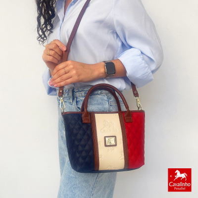 Mala de senhora Cavallinho tricolor matelassé com alças castanhas, exibida por mulher com camisa azul e jeans.