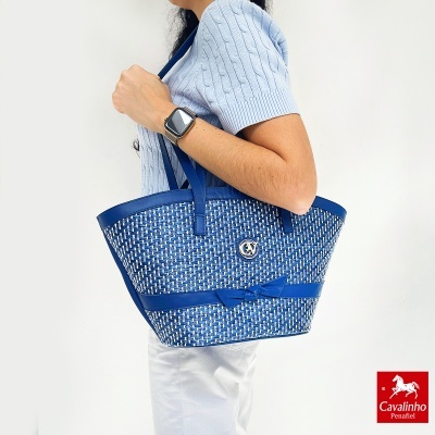 Carteira azul e branca com padrão trançado e laço, usada no ombro de uma mulher com camisa azul clara.