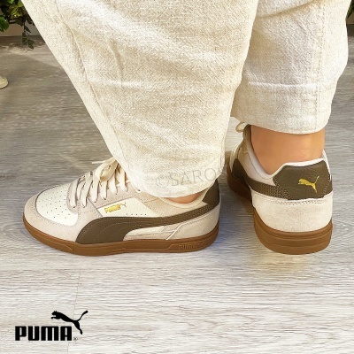 Ténis Puma bege e castanho usados com calças claras em chão de madeira