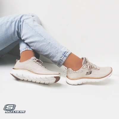 Ténis Skechers bege com sola branca e detalhes dourados usados por pessoa com calças de ganga claras