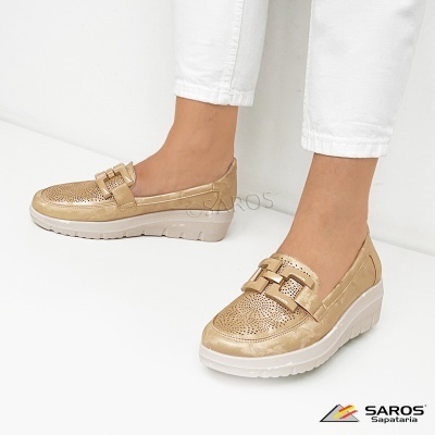 Sapatos mocassim dourados com sola branca usados com calças brancas.