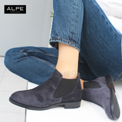 Botas cinzentas de camurça com banda elástica preta, calças de ganga azul, fundo branco.