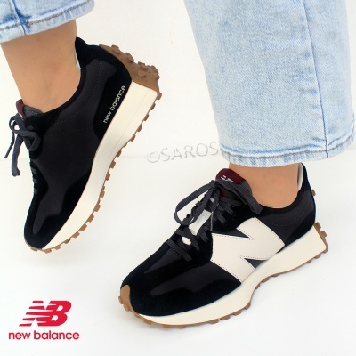 Sapatos desportivos New Balance pretos com detalhe branco e sola castanha, usados com calças de ganga claras.