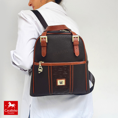 Mochila preta e castanha com fivelas douradas vista de costas numa pessoa de camisa branca