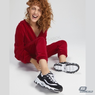 Ténis Skechers pretos e brancos com sola branca usados por modelo com fato de treino vermelho