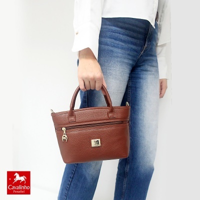 Mala de mão castanha em pele segurada por pessoa com camisa branca e jeans azuis