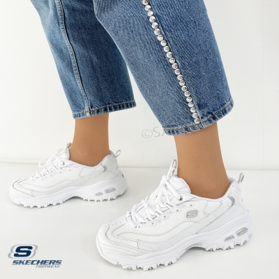 Ténis brancos Skechers usados com calças de ganga azuis com botões